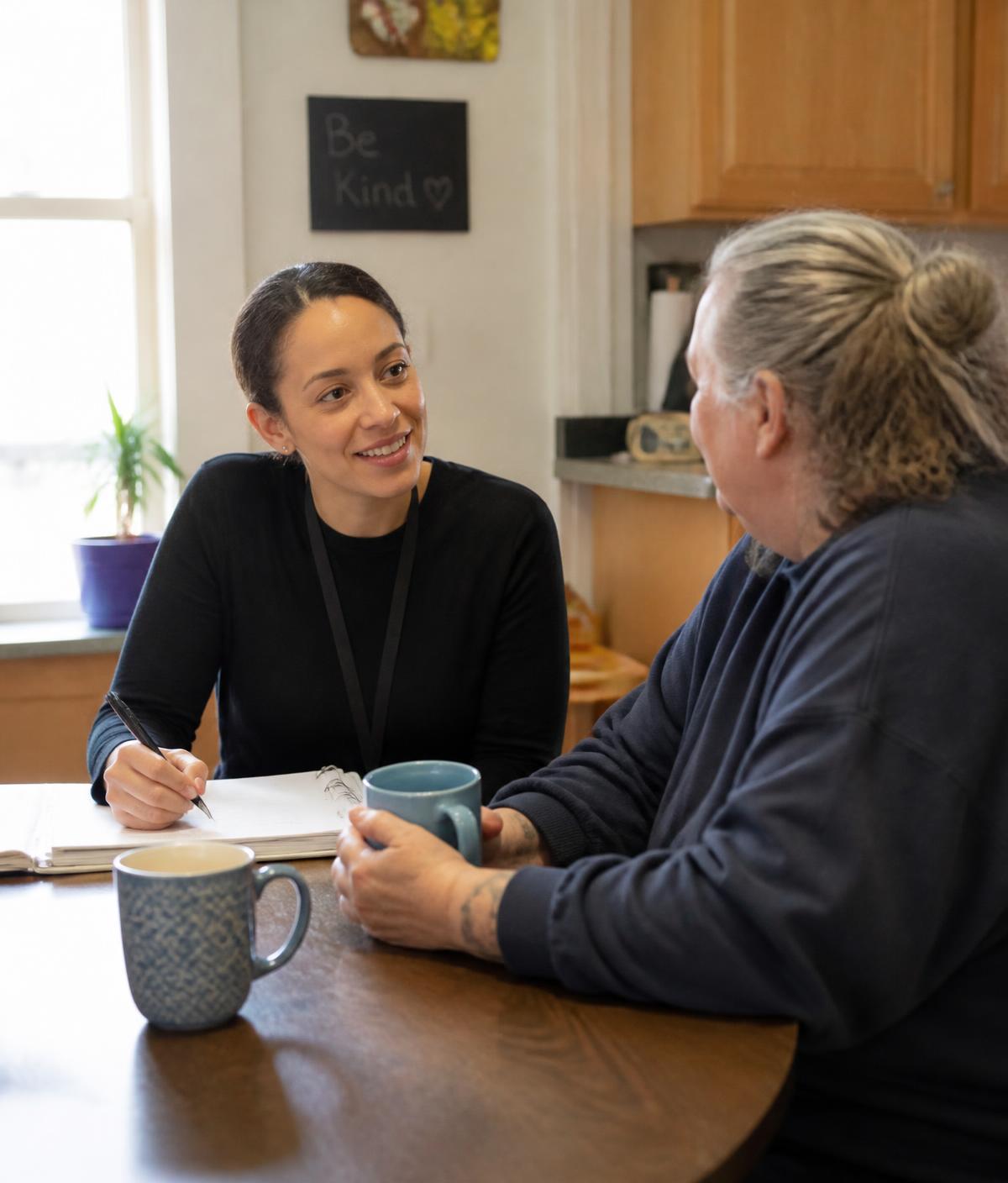 A housing coordinator talking with a resident at a kitchen table